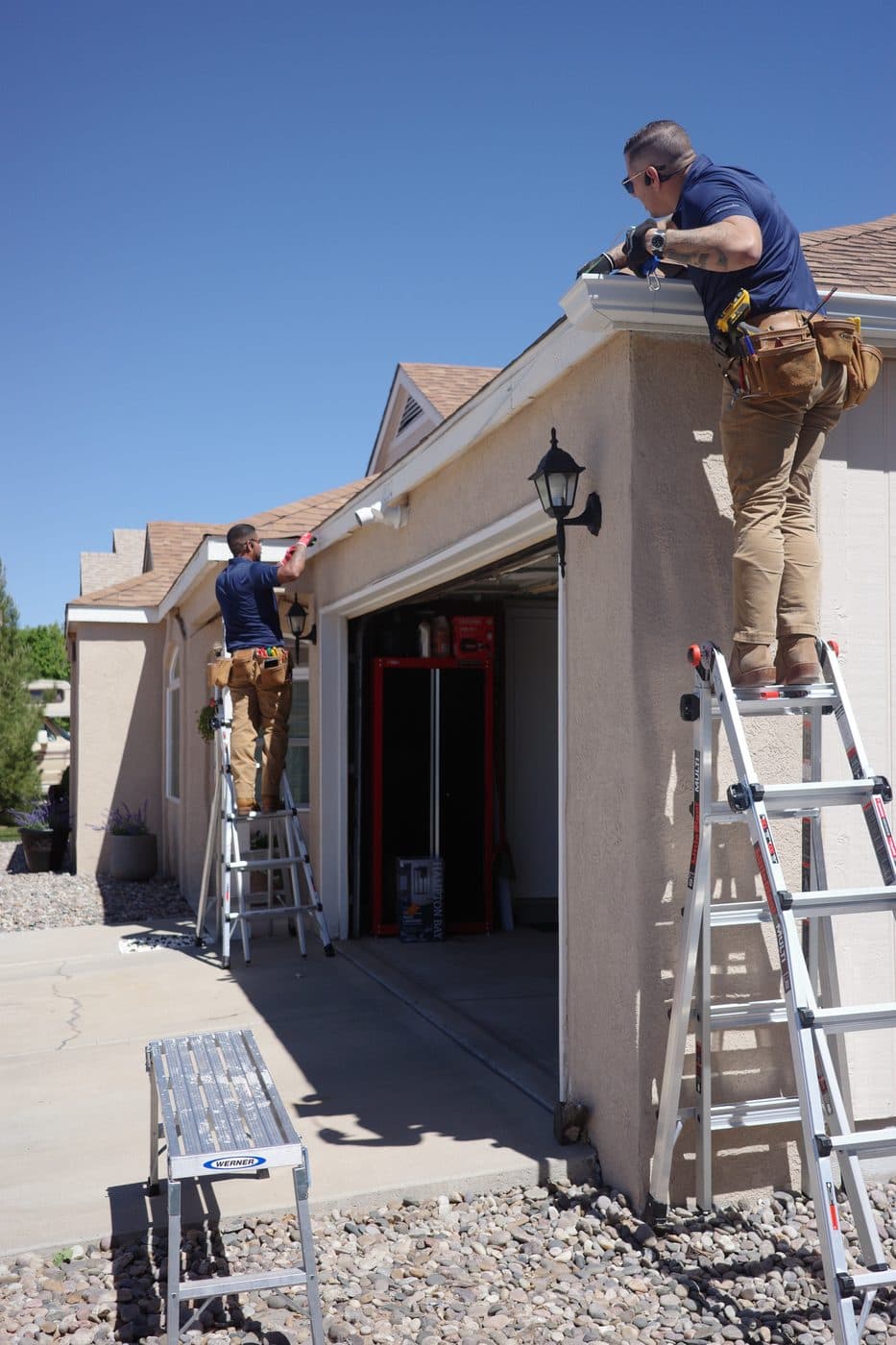 Two technicians installing gutters from ladders on an Albuquerque home