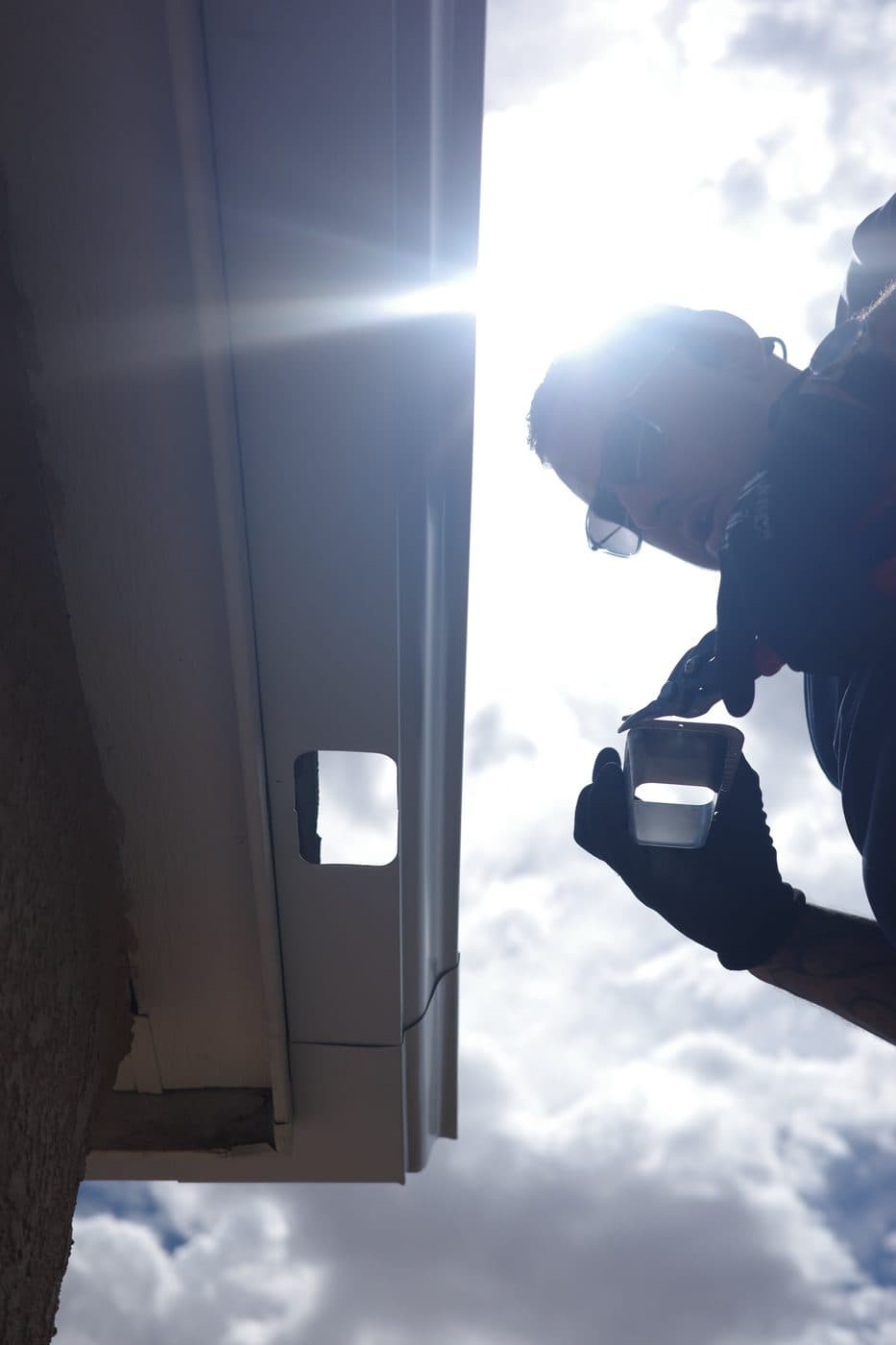 Technician installing a gutter outlet, silhouetted against a bright New Mexico sky