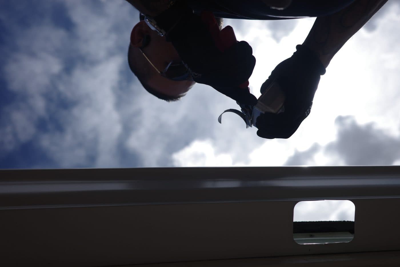 Close-up of a technician fitting a seamless gutter against a blue sky