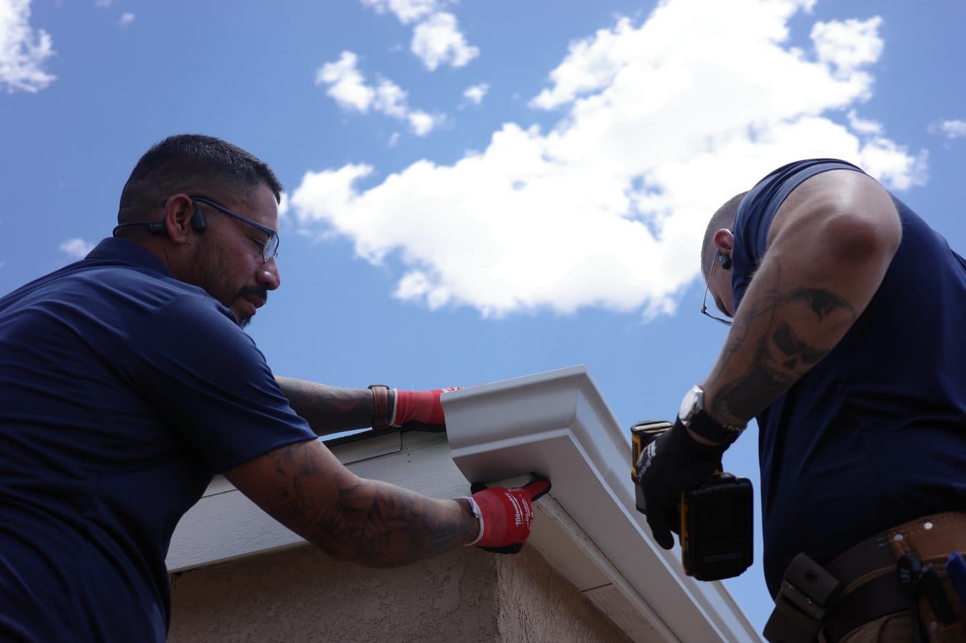 Two technicians fitting a seamless gutter miter on a stucco home